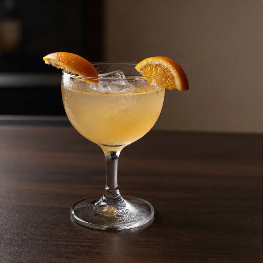 A cocktail with an orange garnish on a dark bar top
