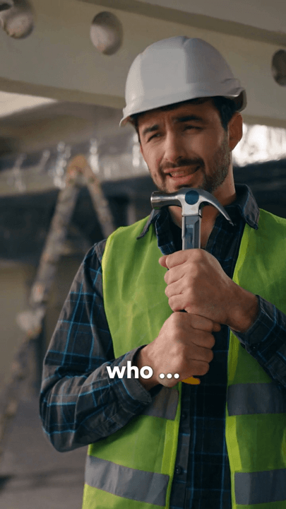 A worker in a hard hat and hi-vis holding a hammer on site